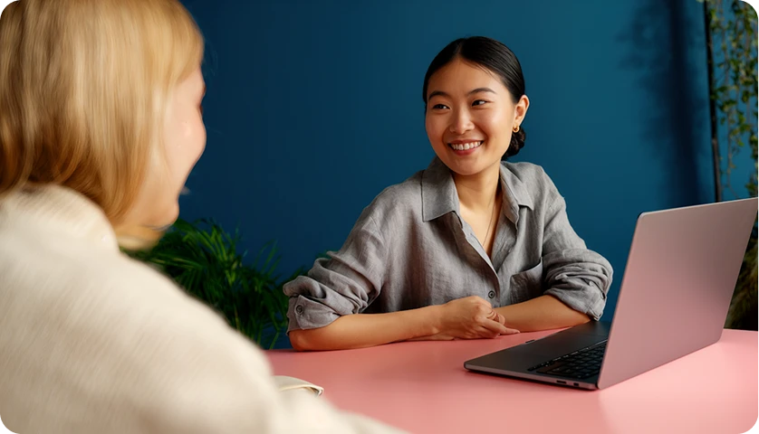 Two colleagues talking across a table beside an open laptop